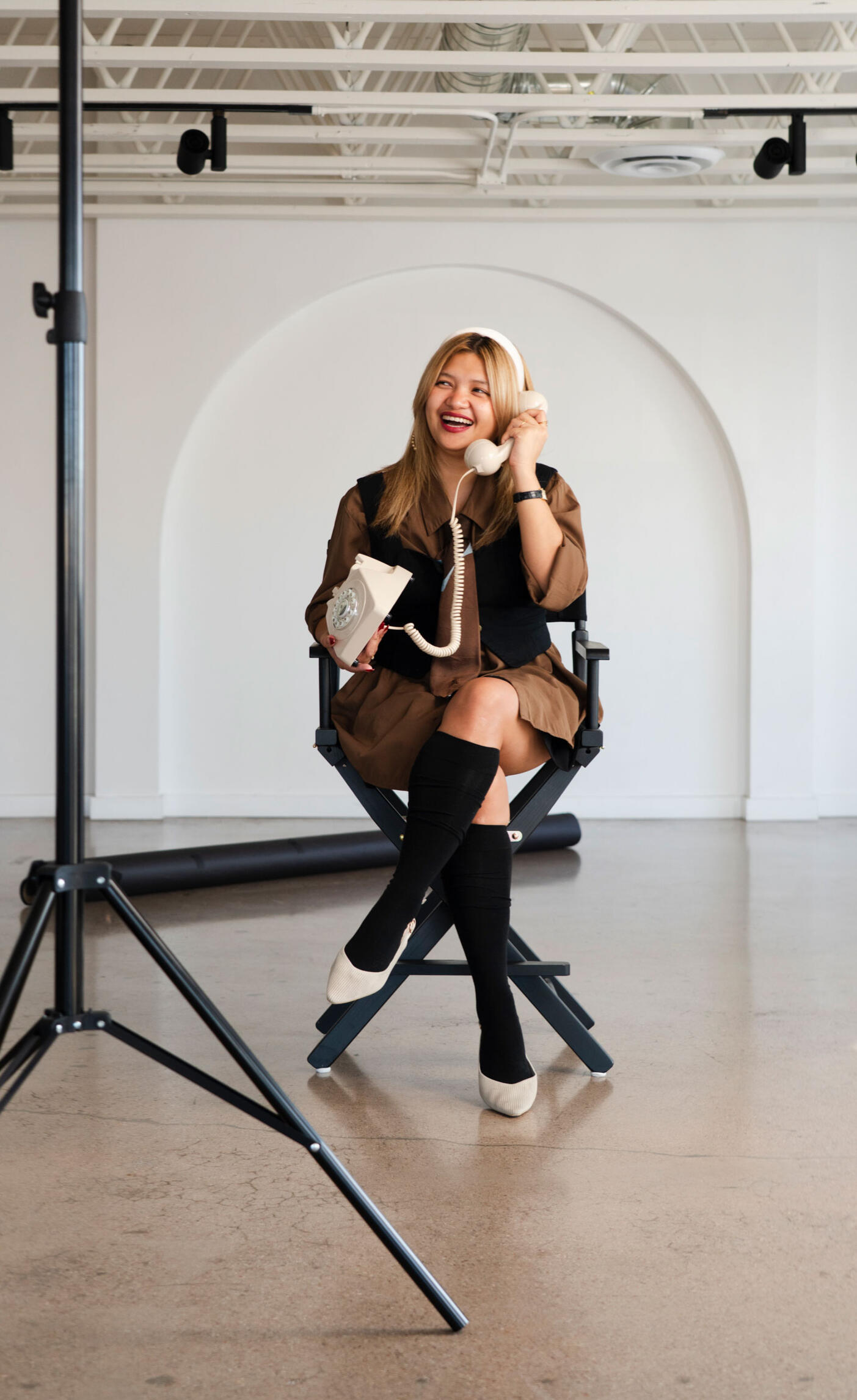 Jazz Digao seated on a director's chair with a telephone on her lap while she laughs and talks to it